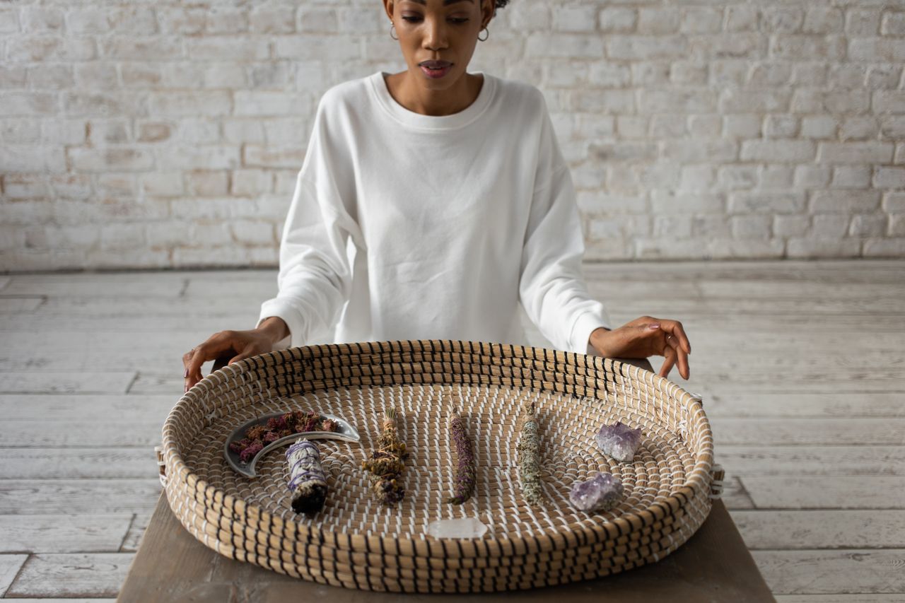 A woman displays a basket containing crystals and sage, enhancing a spiritual atmosphere.