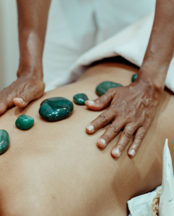 Hands performing a soothing hot stone massage with therapeutic stones on bare back.